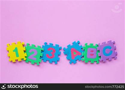 Alphabet puzzle with number puzzle on pink background. Top view
