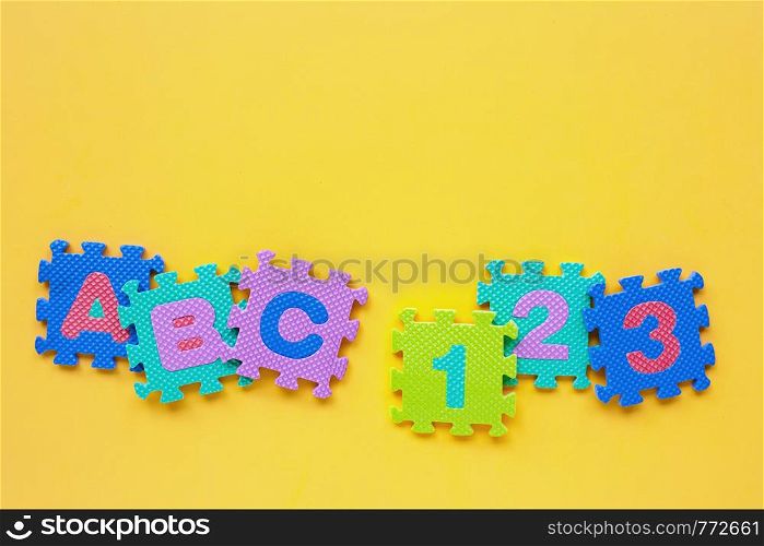 Alphabet puzzle with number puzzle on yellow background. Top view