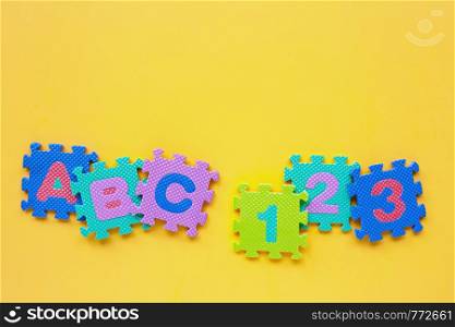 Alphabet puzzle with number puzzle on yellow background. Top view