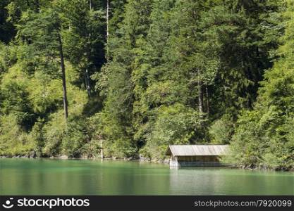 Alpine Lake Alpsee in Ostallgau district of Bavaria, near Neuschwanstein and Hohenschwangau castles. Germany, Europe. Green trees and boating shed.