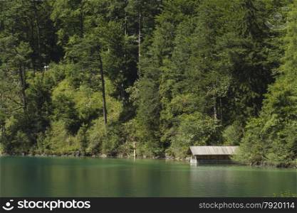 Alpine Lake Alpsee in Ostallgau district of Bavaria, near Neuschwanstein and Hohenschwangau castles. Germany, Europe. Green trees and boating shed.