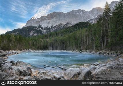 Alpine lake with blue frozen water, surrounded by fir forest and the Alps mountains, near the Eibsee lake, in Bavaria, Germany.