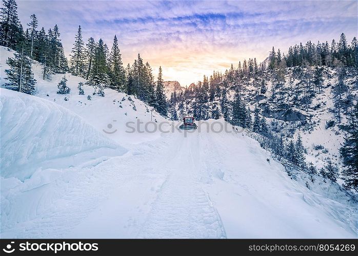 Alpine road mapped out in snow, Austria - Snowy alpine road in the forest of the Austrian Alps mountains, being cleared by a snow removal machine, under a dramatic sky in Ehrwald city.