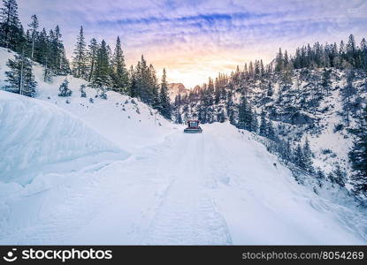 Alpine road mapped out in snow, Austria - Snowy alpine road in the forest of the Austrian Alps mountains, being cleared by a snow removal machine, under a dramatic sky in Ehrwald city.