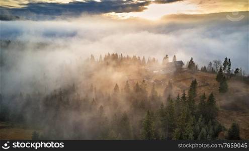 Alpine village. Autumn rural landscape. Cold November morning. Morning fog in mountain valley. Forest covered by low clouds. Misty fall woodland. Picturesque resort Carpathians range, Ukraine, Europe.