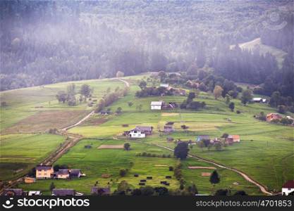 Alpine village in mountains. Smoke and haze over the hills in Carpathians.