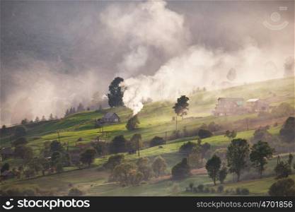 Alpine village in mountains. Smoke, bonfire and haze over the hills in Carpathians.
