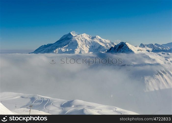 Alpine winter mountain landscape with low clouds. French Alps covered with snow in sunny day. Val-d'Isere, France