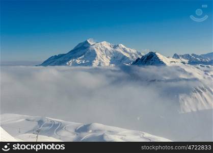Alpine winter mountain landscape with low clouds. French Alps covered with snow in sunny day. Val-d'Isere, France
