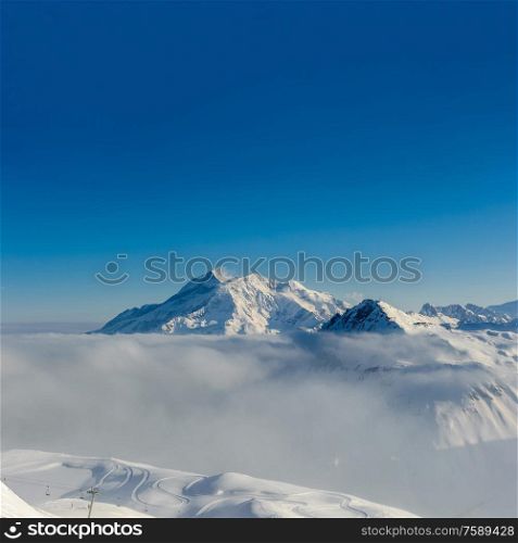 Alpine winter mountain landscape with low clouds. French Alps covered with snow in sunny day. Val-d&rsquo;Isere, France
