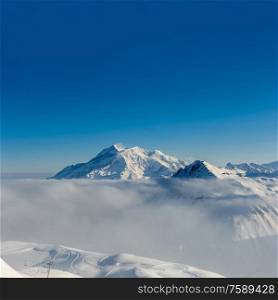 Alpine winter mountain landscape with low clouds. French Alps covered with snow in sunny day. Val-d&rsquo;Isere, France