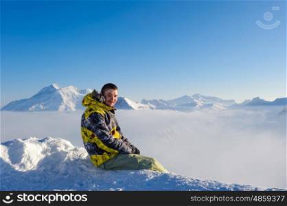 Alpine winter mountain landscape with man sitting above low clouds. French Alps covered with snow in sunny day. Val-d'Isere, France