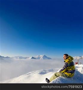 Alpine winter mountain landscape with man sitting above low clouds. French Alps covered with snow in sunny day. Val-d&rsquo;Isere, France