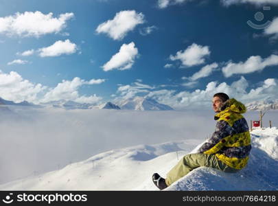 Alpine winter mountain landscape with man sitting above low clouds. French Alps covered with snow in sunny day. Val-d’Isere, France