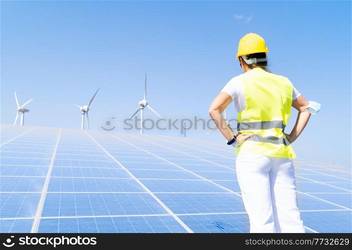 alternative energy concept - back of woman in covid mask standing in front of solar panels, green energy and eco friedly industry concept. alternative energy concept