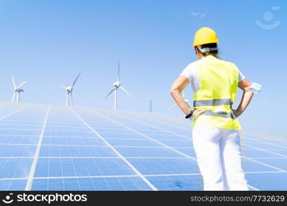 alternative energy concept - back of woman in covid mask standing in front of solar panels, green energy and eco friedly industry concept. alternative energy concept