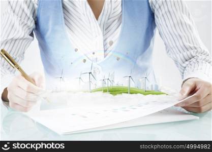Alternative energy concept. Close view of businesswoman writing with pen and wind generators on papers
