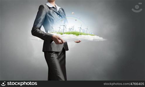 Alternative energy concept. Wind turbines on meadow in woman hands against sky background