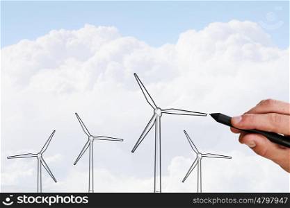Alternative energy. Person hand drawing windmills on sky background