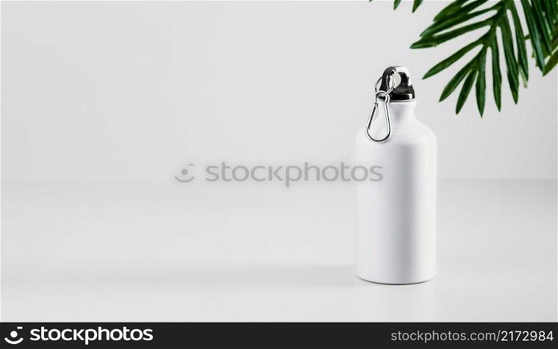 Aluminum water bottle for sports or fitness on a neutral gray background, palm leaves in the background. Place for text. Reuse and recycling of materials