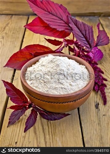 Amaranth flour in a clay bowl and purple amaranth flower on the background of wooden boards