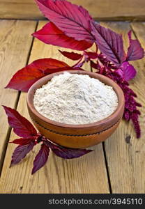 Amaranth flour in a clay bowl and purple amaranth flower on the background of wooden boards