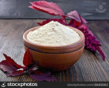 Amaranth flour in a clay bowl, purple amaranth flower against the dark wooden board