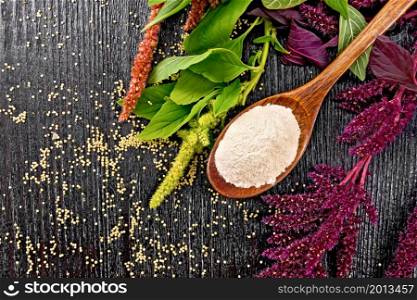 Amaranth flour in a spoon, brown, green and purple flowers and leaves of a plant, seeds on wooden board background from above