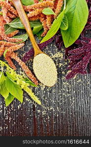 Amaranth groats in a spoon, red, burgundy and green inflorescences with leaves on the background of a wooden board from above