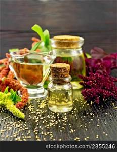 Amaranth oil in a glass bottle, gravy boat and jar, amaranth seeds, brown, green and purple flowers and leaves of the plant on the background of a wooden board