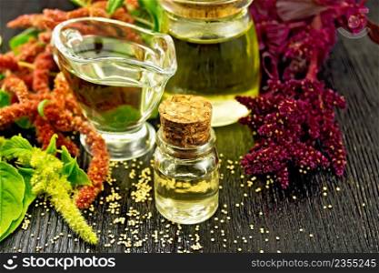 Amaranth oil in a glass bottle, gravy boat and jar, brown, green and purple flowers and leaves of the plant on the background of wooden board
