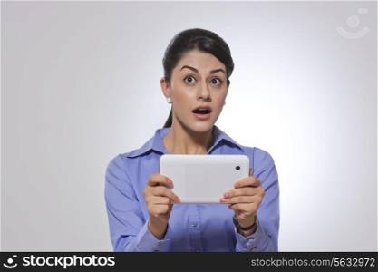 Amazed businesswoman holding digital tablet over gray background