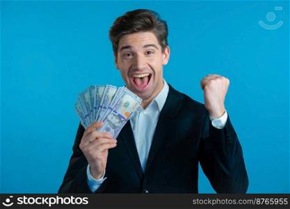 Amazed happy excited businessman with money - U.S. currency dollars banknotes on blue studio wall. Symbol of success, gain, victory. Amazed happy excited businessman with money - U.S. currency dollars banknotes on blue studio wall. Symbol of success, gain, victory.