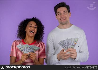 Amazed happy excited interracial couple showing money - USD currency dollars banknotes on purple wall. Symbol of success, gain, victory. African woman and white man win lottery. High quality photo. Amazed happy excited interracial couple showing money - USD currency dollars banknotes on purple wall. Symbol of success, gain, victory. African woman and white man win lottery.