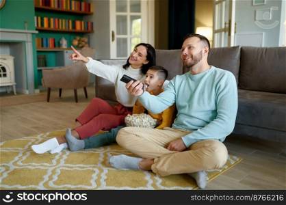 Amazed parents and curious kid watching tv program sitting on floor in living room at home. Amazed parents and curious kid watching tv program at home