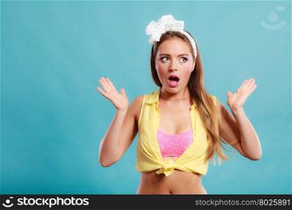 Amazed surprised pin up girl with mouth wide open. Portrait of astonished young woman with bow on blue background.