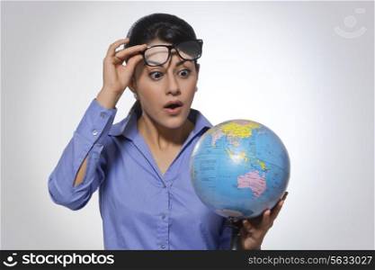 Amazed young businesswoman looking at globe over glasses against gray background