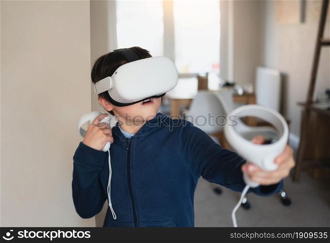 Amazed young kid wearing virtual reality goggles. Emotional Boy playing video games looking in VR headset. Portrait of Mixed race boy experiencing 3D gadget in living room.