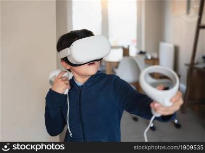 Amazed young kid wearing virtual reality goggles. Emotional Boy playing video games looking in VR headset. Portrait of Mixed race boy experiencing 3D gadget in living room.