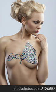 amazing blonde woman with creative blonde hair-style posing and shows her naked breast with glossy decoration on skin