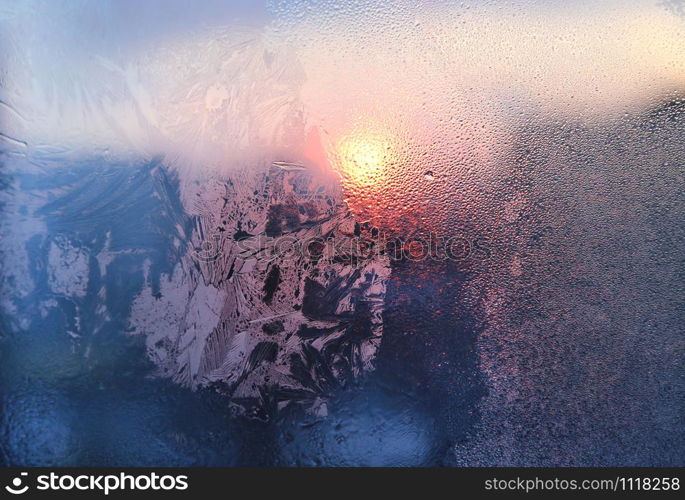 Amazing ice pattern and water drops on a frozen window glass on a sunny winter morning, close-up natural texture