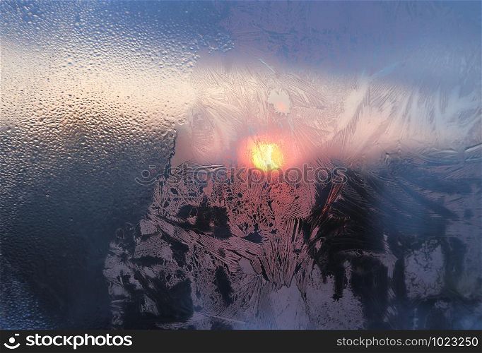 Amazing ice patterns and water drops on a frozen window pane on a sunny winter morning, closeup natural texture