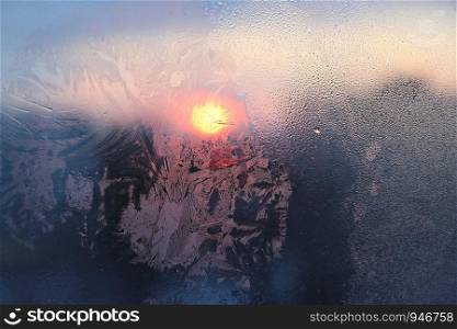 Amazing ice patterns and water drops on a frozen window pane on a sunny winter morning, closeup natural texture