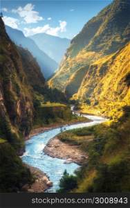 Amazing landscape with high Himalayan mountains, beautiful curving river, green forest, blue sky with clouds and yellow sunlight in autumn in Nepal. Mountain valley. Travel in Himalayas. Nature