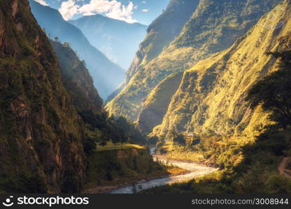 Amazing landscape with high Himalayan mountains, beautiful curving river, green forest, blue sky with clouds and yellow sunlight in autumn in Nepal. Mountain valley. Travel in Himalayas. Nature