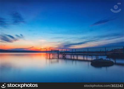 Amazing long exposure sunset on the lake with a bench on the wooden pier.