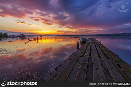 Amazing mood sunset at a lake coast with a boat at a wooden pier