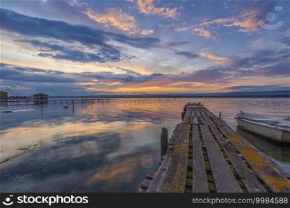 Amazing mood sunset at a lake coast with a boat at a wooden pier