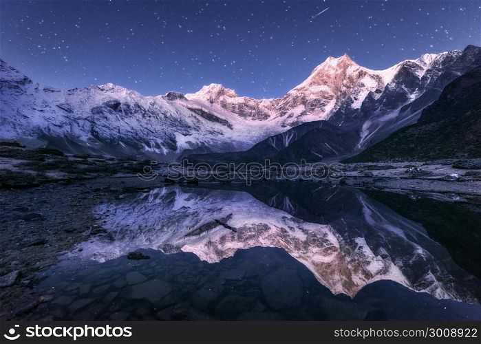 Amazing night scene with himalayan mountains and mountain lake at starry night in Nepal. Landscape with high rocks with snowy peak and sky with stars reflected in water. Beautiful Manaslu, Himalayas