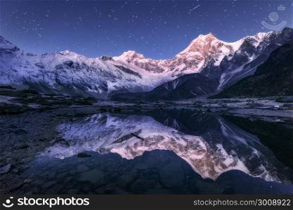 Amazing night scene with himalayan mountains and mountain lake at starry night in Nepal. Landscape with high rocks with snowy peak and sky with stars reflected in water. Beautiful Manaslu, Himalayas